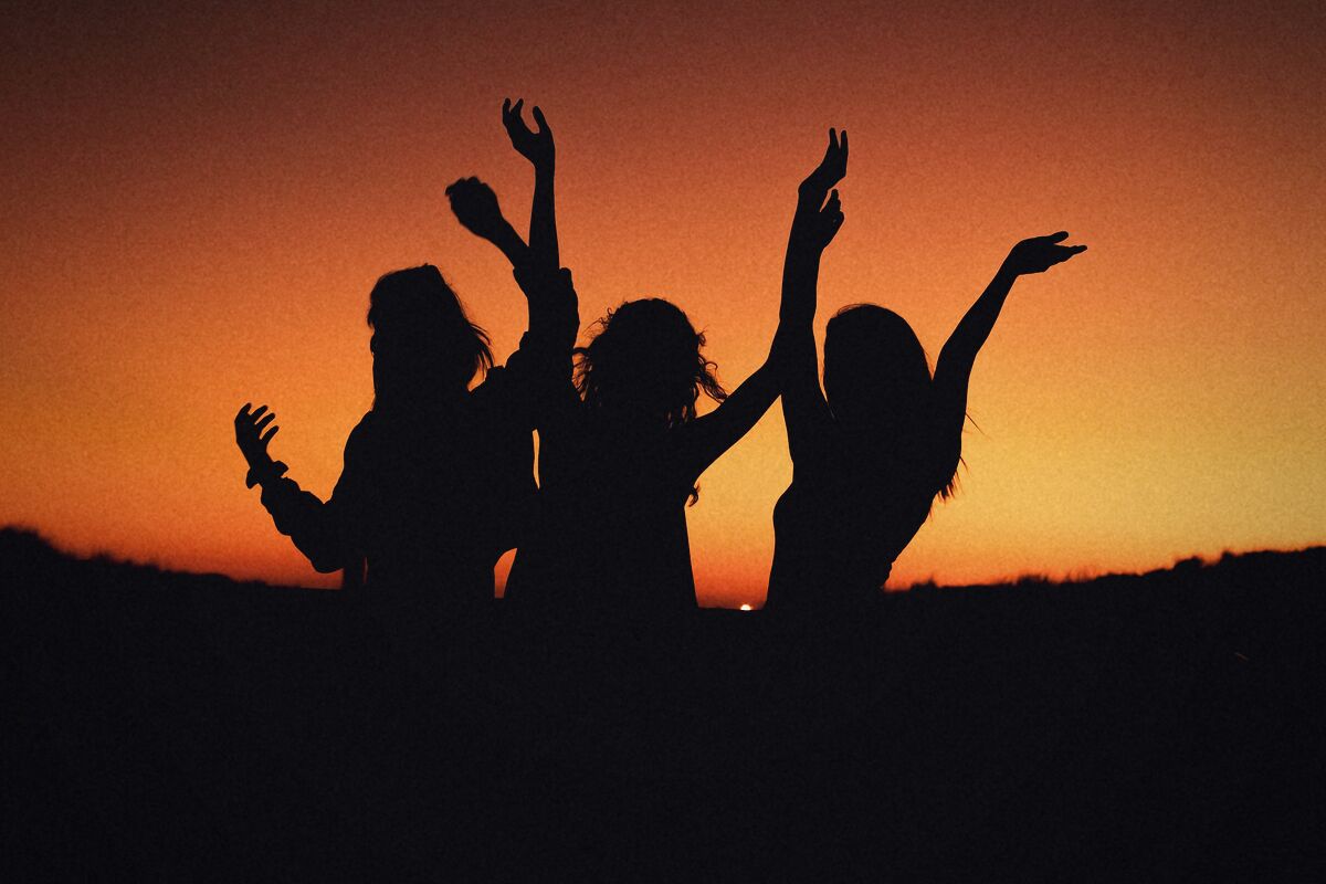 Silhouettes de danseuses les bras levés devant le ciel orange